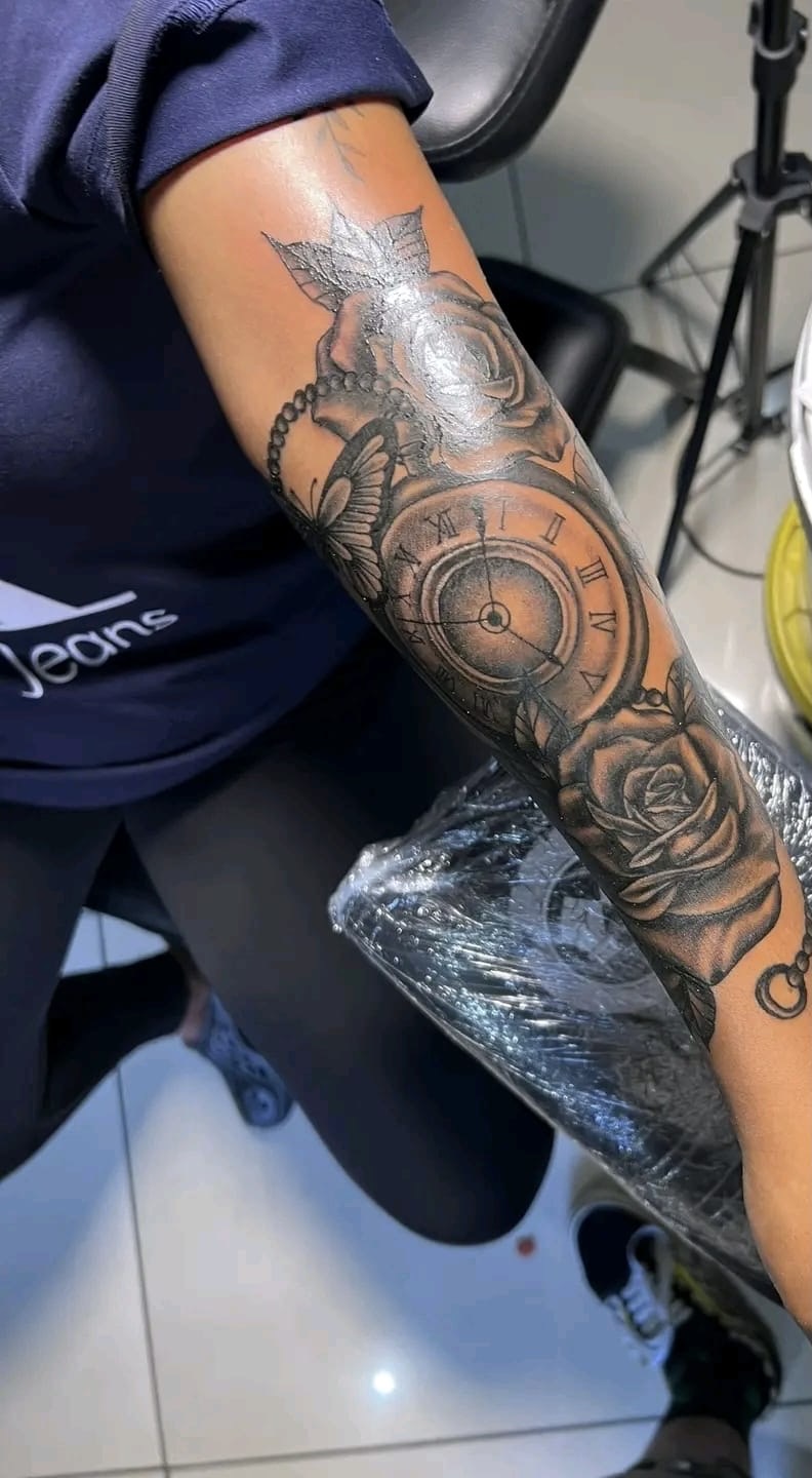 Black-and-grey roses, clock and butterfly tattoo on an arm